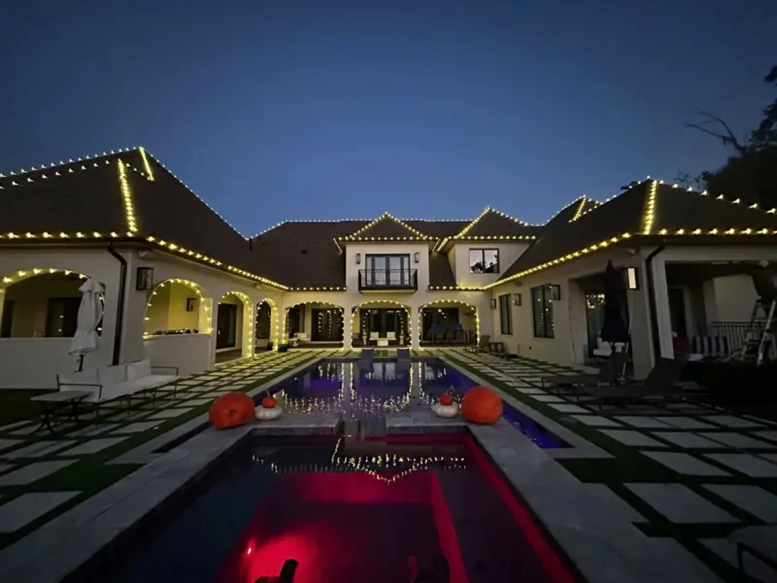 Estate home and pool courtyard outlined in warm white Christmas lights at dusk